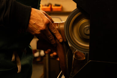 Mains d’un cordonnier travaillant à la réparation d’une chaussure dans son atelier, illustrant le savoir-faire artisanal et l’expertise des professionnels de la réparation.